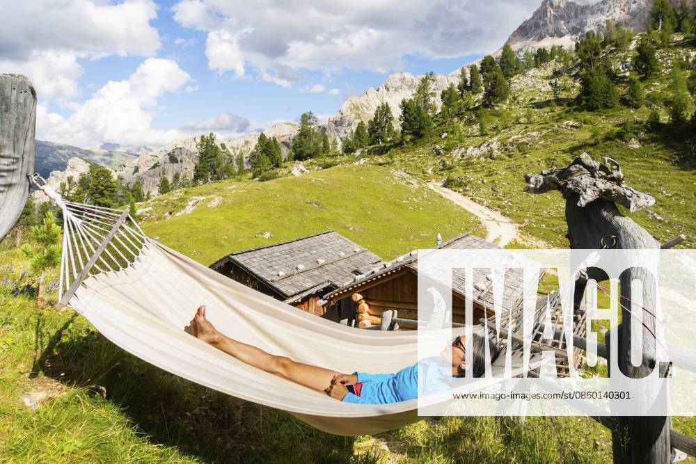 Wanderin ruht sich in einer Hängematte auf einer Berghütte auf dem Tre Cime Weg in den Dolomiten aus und genießt die alpine Landschaft, ein Wellness Abenteuer und eine Wanderpause Female hiker resting in hammock at mountain hut on Tre Cime trail in Dolomites enjoying alpine scenery wellness adventure and hiking break