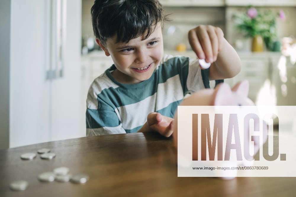 A smiling boy puts a coin into a pink piggy bank at home model released, Symbolfoto property released, ANAF06326