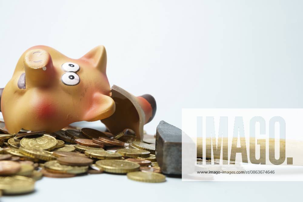 Kaputtes Sparschwein, das auf einem Stapel Euro Münzen liegt, daneben ein Hammer, der Finanzkrise und Schulden symbolisiert Broken piggy bank lying on a pile of euro coins, with a hammer next to it, symbolizing financial crisis and debt