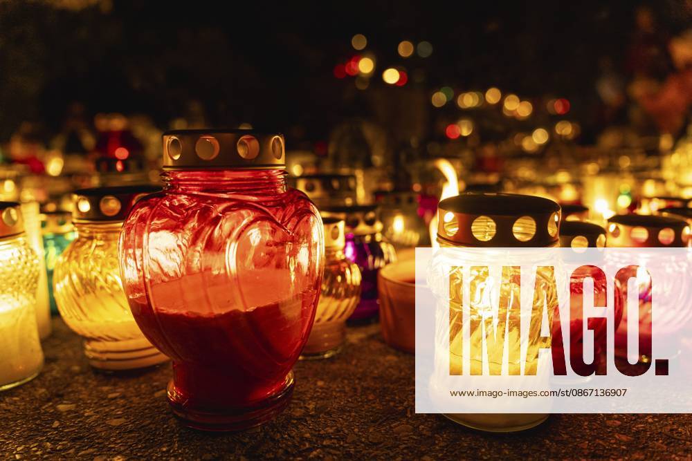 Herzförmige Kerze zwischen glühenden Kerzen in der Nacht auf dem Friedhof an Allerheiligen, Totentag oder Gedenktag. Eine riesige Anzahl bunter brennender Kerzen und Lampen auf einem Friedhof während der Feierlichkeiten zu Allerheiligen. Warschau, Polen Heart-shaped candle among glowing candles in the night at cemetery on all saints day, day of the dead, or memorial day. A huge number of multicolored burning candles and lamps at a cemetery during All Saints Day celebrations. Warsaw, Poland