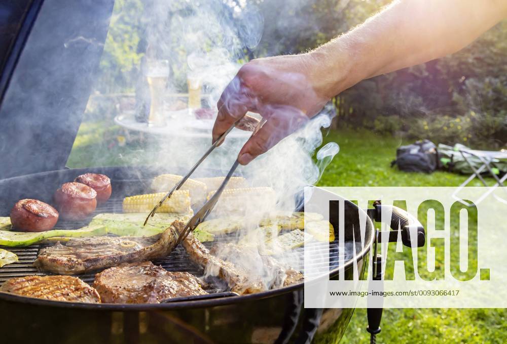 DEU, Germany, Münsingen, Baden Württemberg, 24 08 2019 Barbecue in the garden Steaks of beef, leg of lamb, neck of pork, tomatoes, corn and courgettes lie on the grill