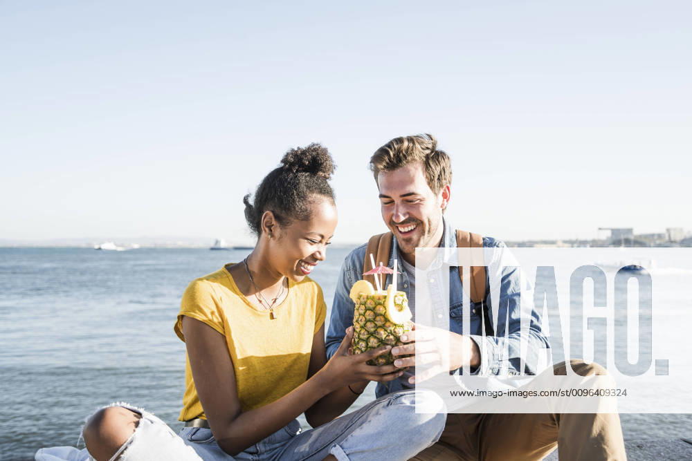 Happy young couple sitting at the waterfront sharing a drink in a pineapple, Lisbon, Portugal model released Symbolfoto UUF19849