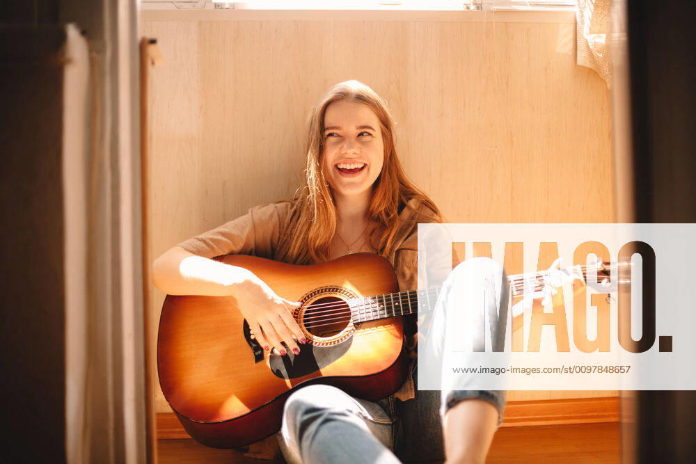 Cheerful young woman holding guitar while sitting on balcony floor ,model released, Symbolfoto CR_DMBE200115-273298-01
