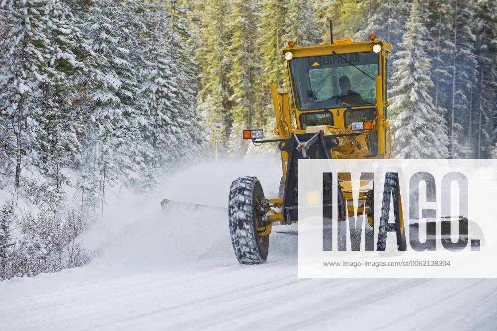 Grader plowing snow from the road surface on a winter day on a back ...