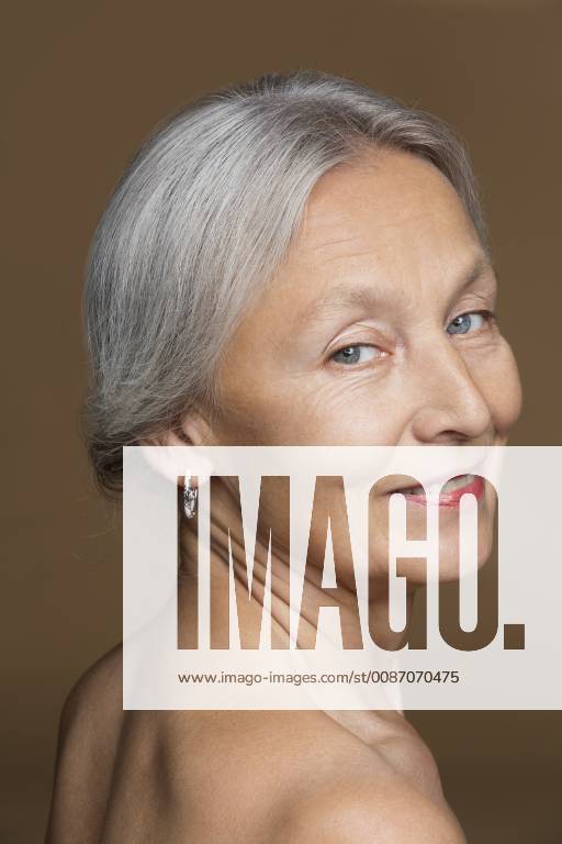 Portrait Of Naked Senior Woman With Grey Hair In Front Of Brown Background Model Released