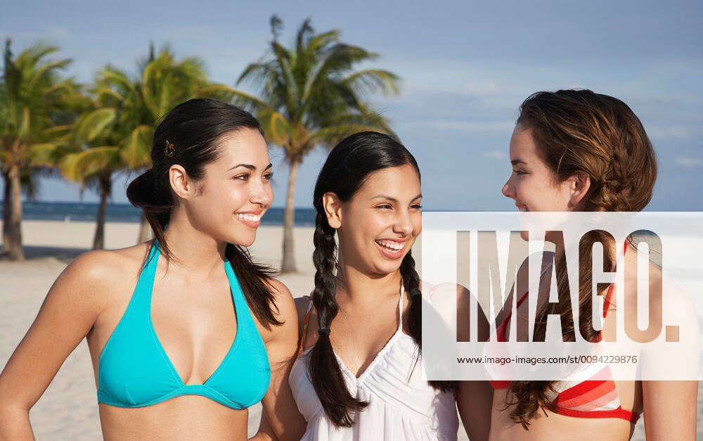 Three teenage girls (16-17) wearing bikinis standing on beach